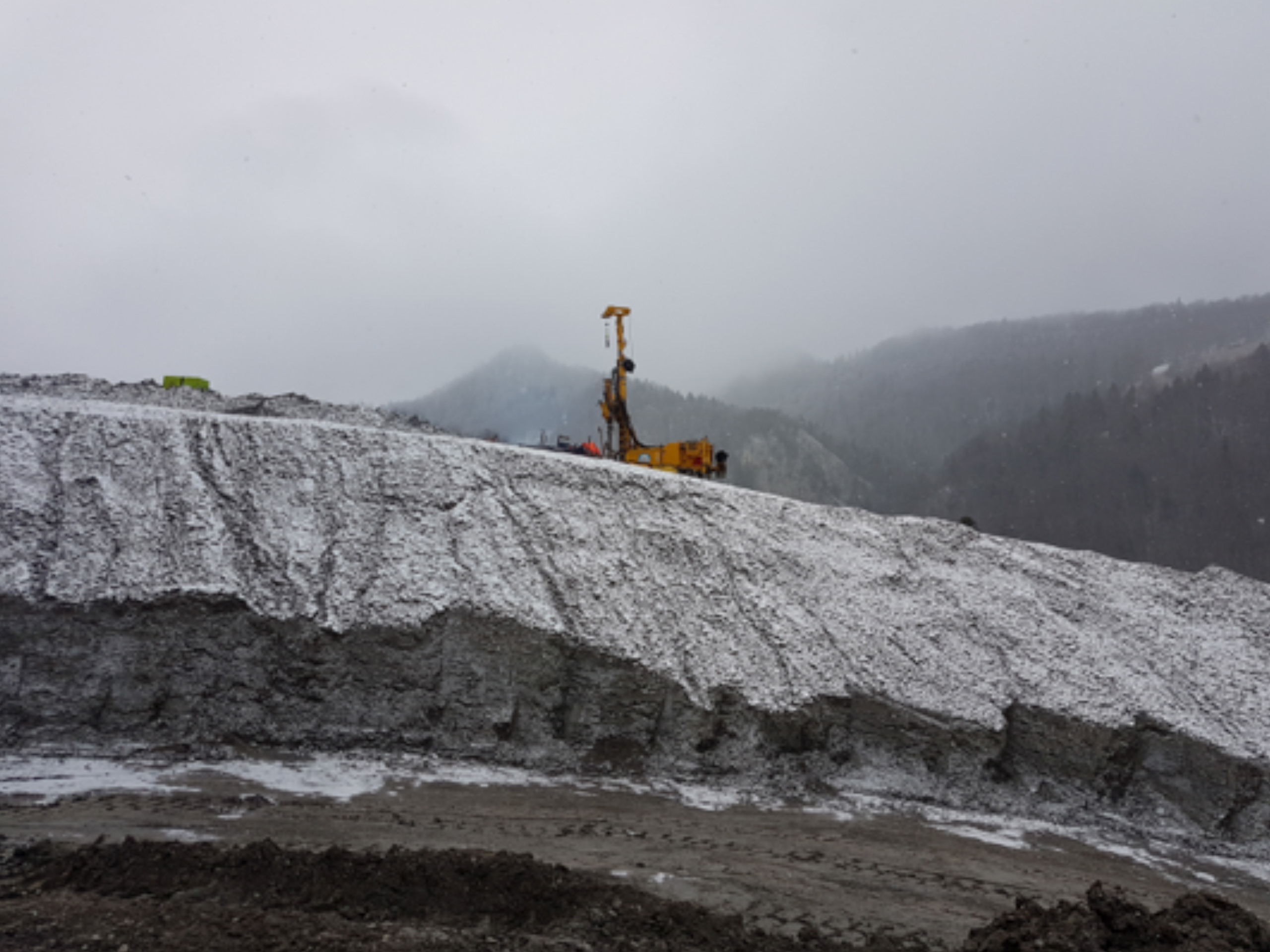 Leicht schneebedeckter Deponie Berg mit grosser Bohrmaschine